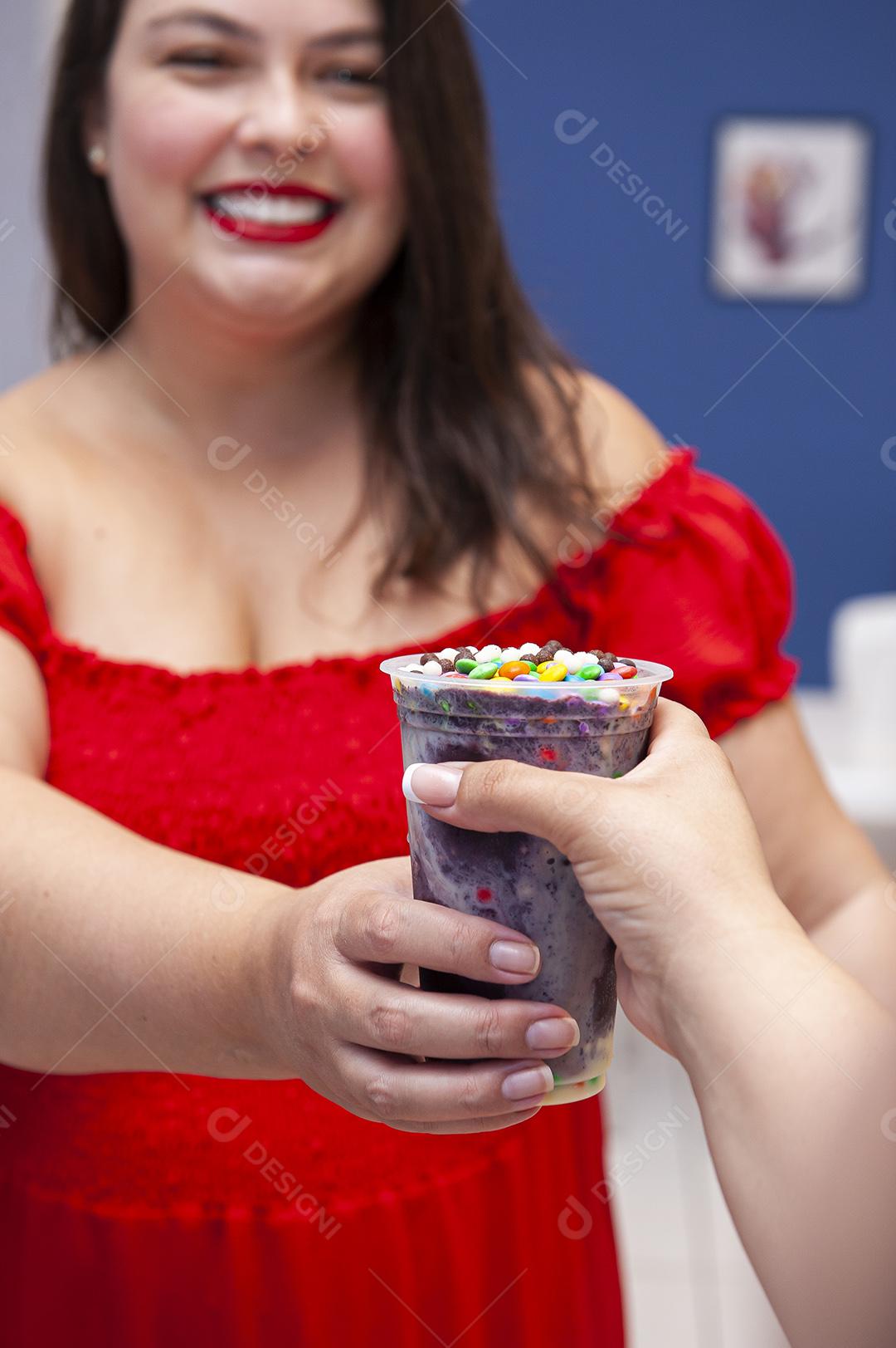 Menina bonita e sorridente recebendo um copo de açaí congelado