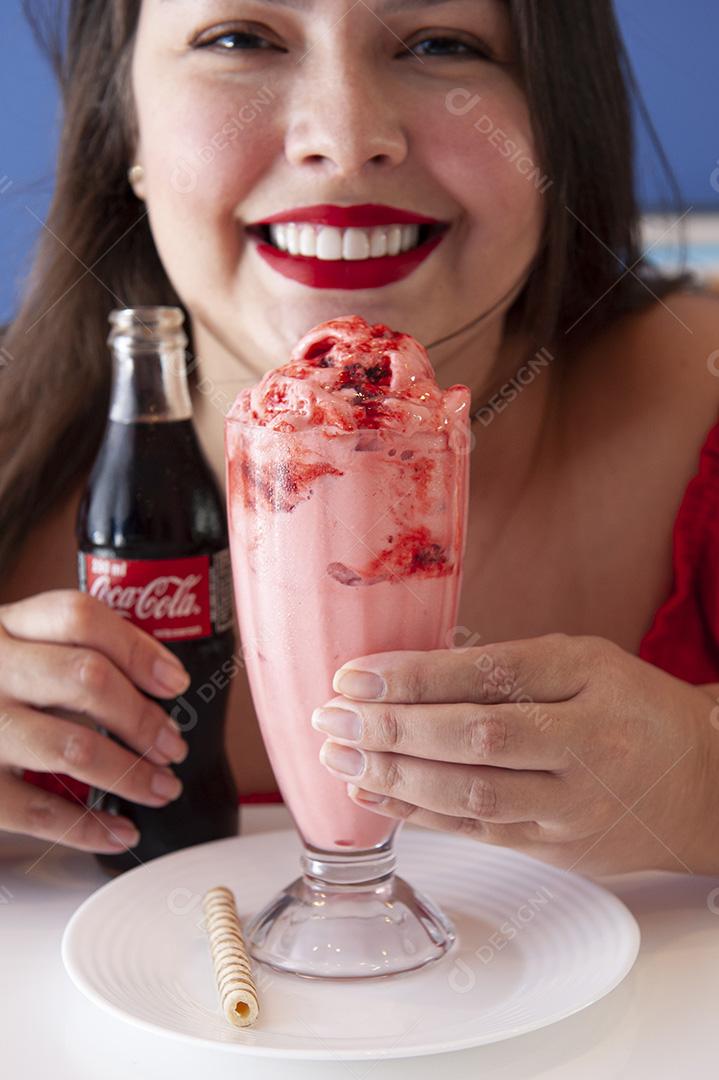 Menina bonita e sorridente tomando uma xícara de sorvete com coca cola