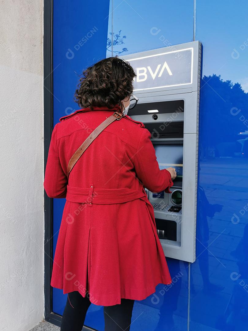 Málaga, Espanha - 11 de março de 2021: Mulher mascarada tentando sacar dinheiro do caixa eletrônico durante a pandemia.