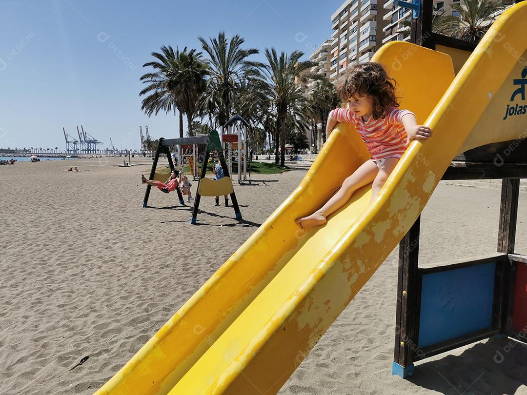 Málaga, Espanha - 04 DE ABRIL DE 2021: Vista de uma garotinha descendo o escorregador de praia no verão.