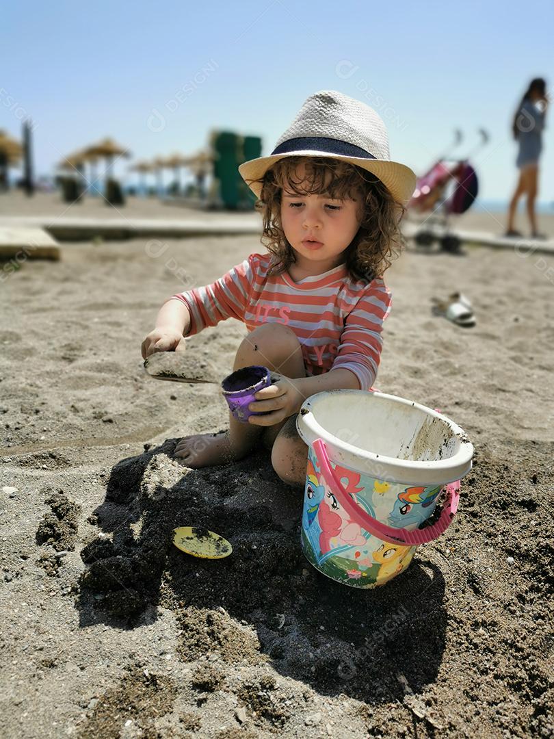 Málaga, Espanha - 22 DE ABRIL DE 2021: Vista de uma linda garota brincando com um balde de areia na praia.