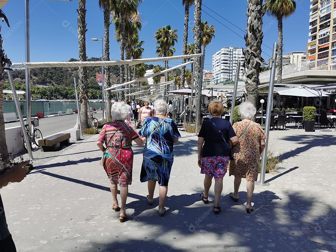 Vista de 4 amigas mais velhas andando pelo porto de Málaga no verão.