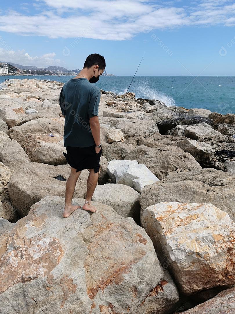 Jovem de pé nas rochas com máscara olhando para o celular no verão europeu