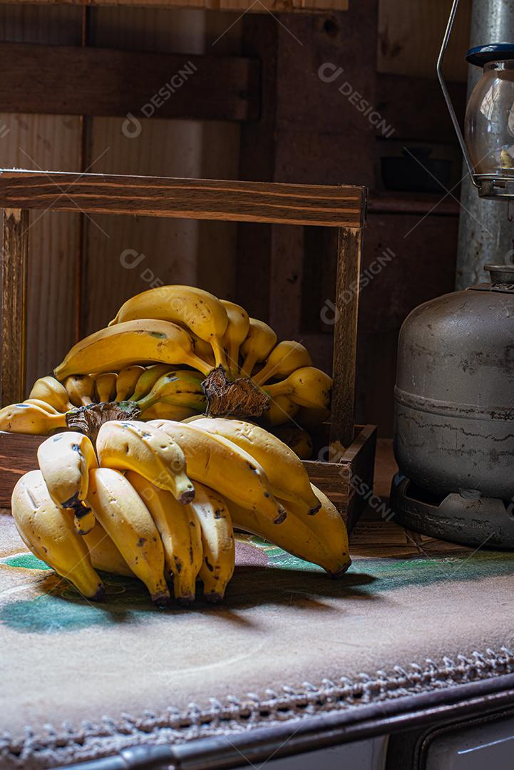 Cachos de banana, em cima de um fogão velho com toalha bordada e ao lado de um lampião a gás.