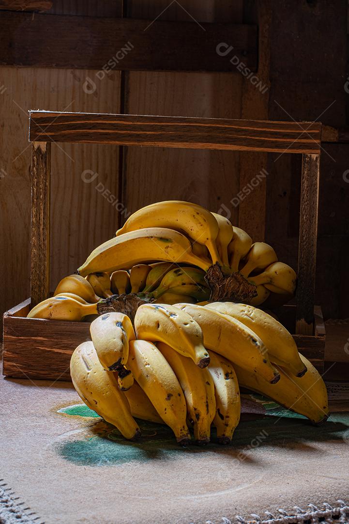 Cachos de banana, em cima de um fogão velho com toalha bordada e ao lado de um lampião a gás.