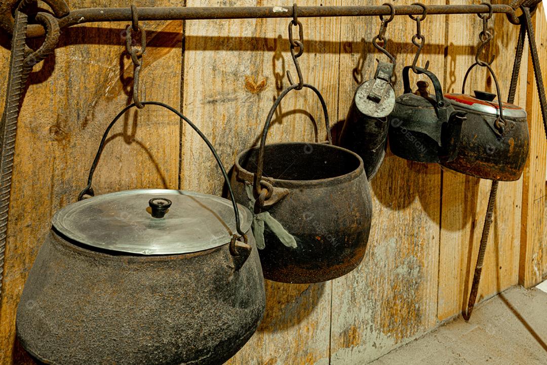 Panelas de ferro antigas penduradas em um suporte de ferro na cozinha da fazenda