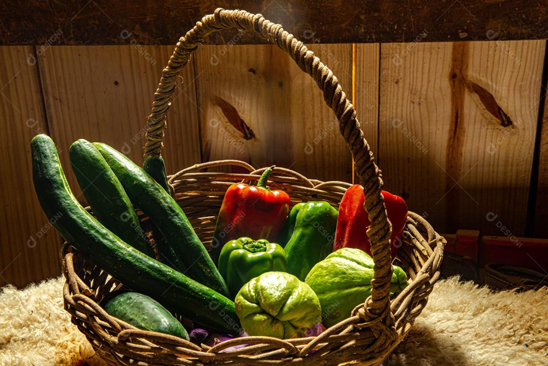 Cesta de palha com produtos orgânicos: pepino, pimentão verde, vermelho