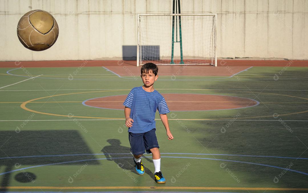 Menino chutando bola de futebol na quadra de esportes