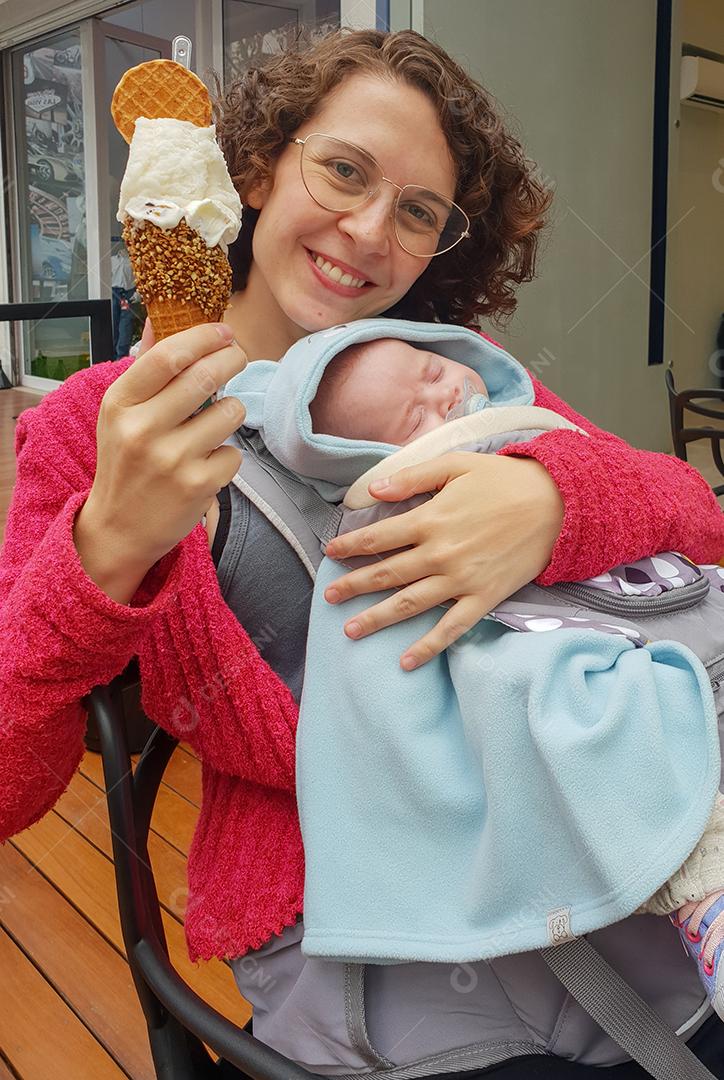 Mãe descansando tomando sorvete com bebê no colo.