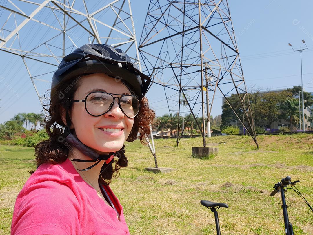 Jovem mulher sorrindo na ciclovia com capacete em sua bicicleta.