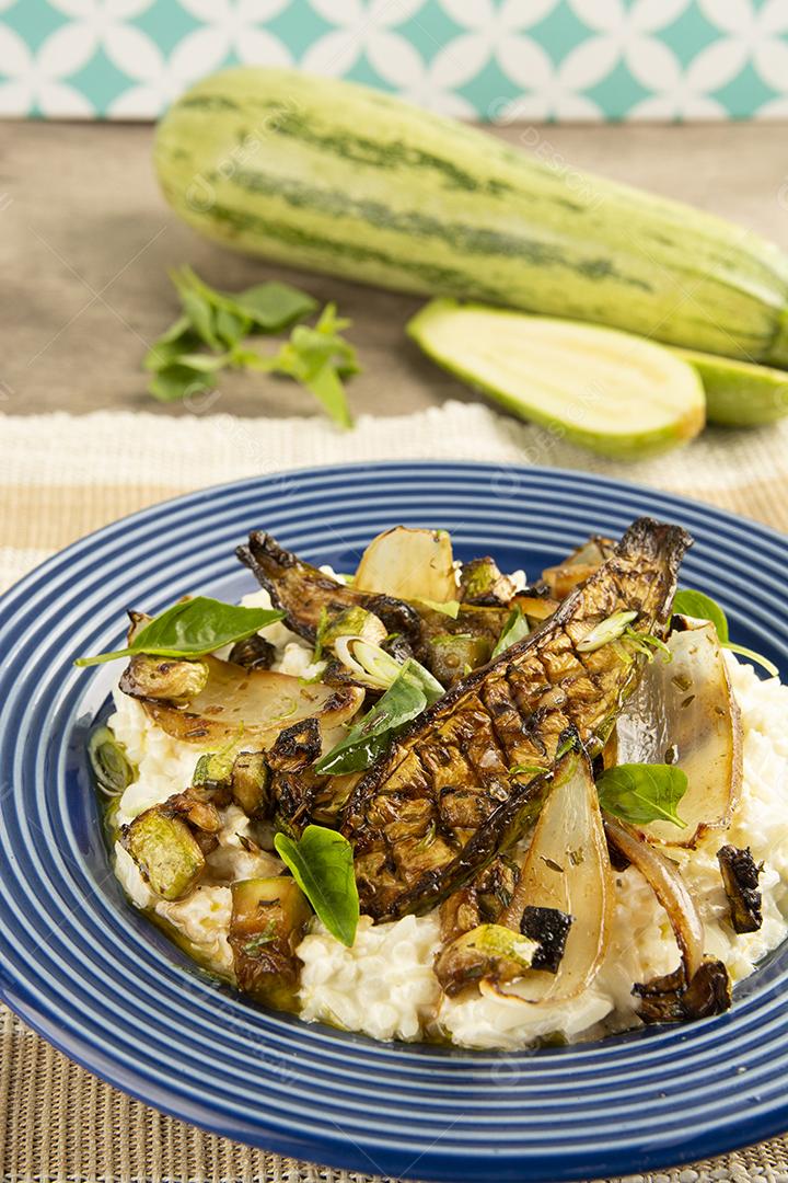 Abobrinha grelhada, arroz, cebola e manjericão sobre um prato azul com abobrinha crua.