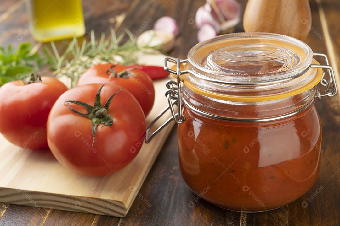 Tomate, molho de tomate, alho, pimentão e ervas sobre a mesa de madeira.