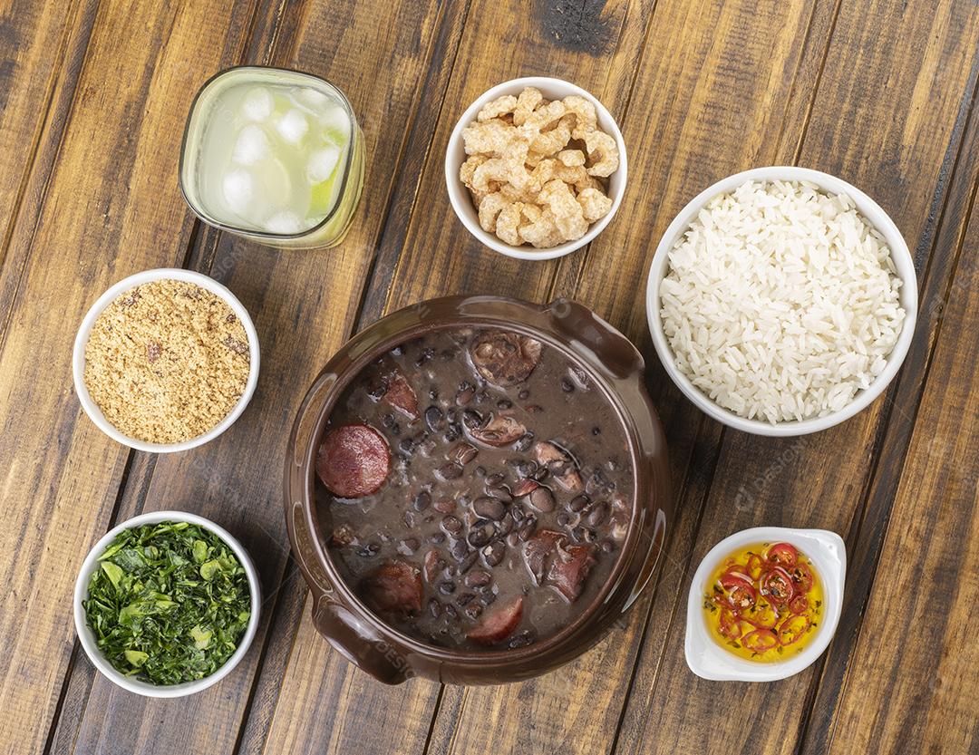 Tradicional feijoada brasileira com couve, farinha de mandioca, arroz, pimenta, torresmo e caipirinha.
