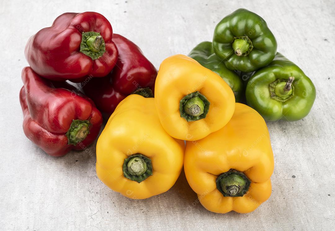 Pimentões verdes, vermelhos e amarelos sobre fundo rústico.