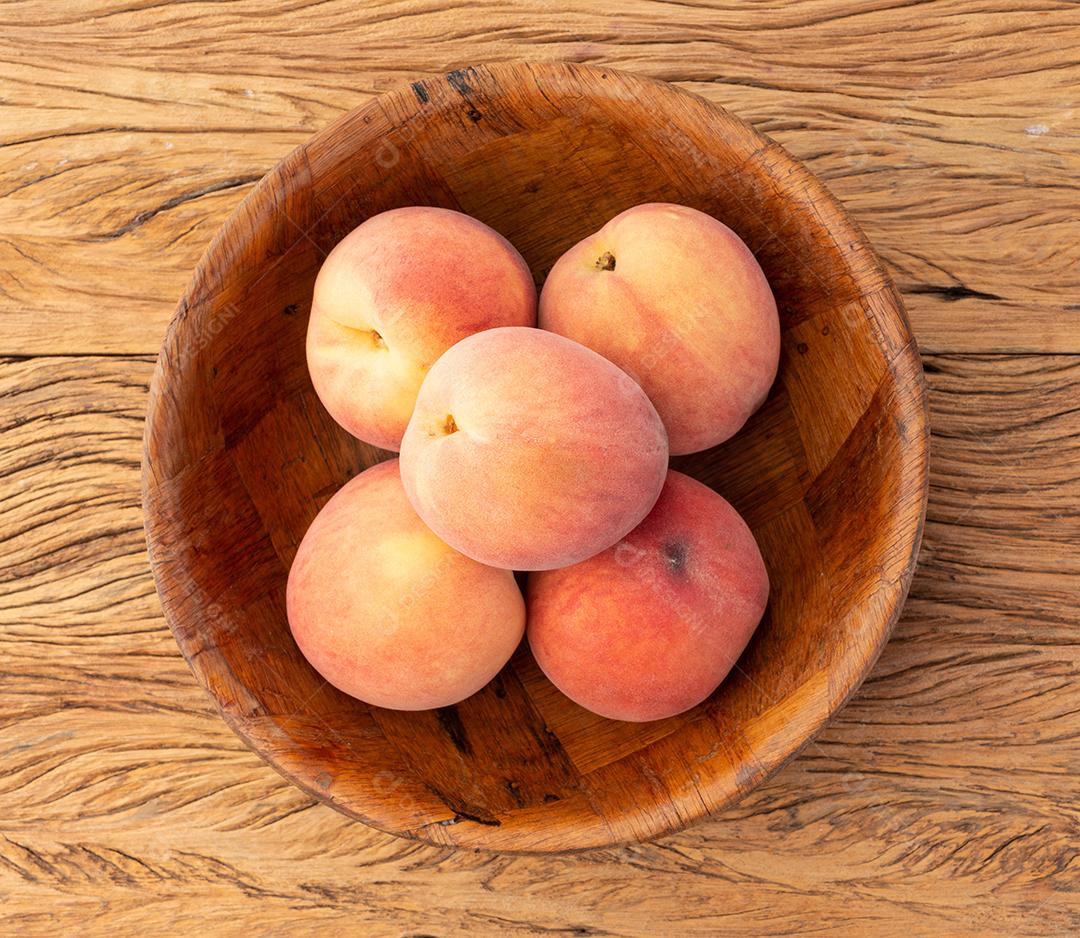 Pêssegos em uma tigela sobre a mesa de madeira.