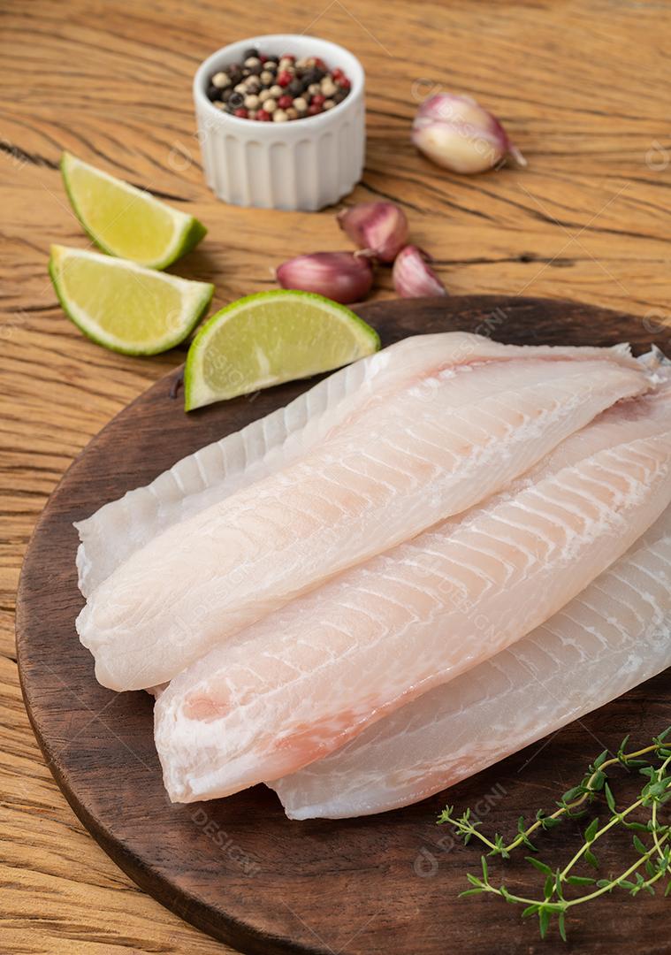 Filé de peixe tilápia cru com temperos sobre fundo de pedra.