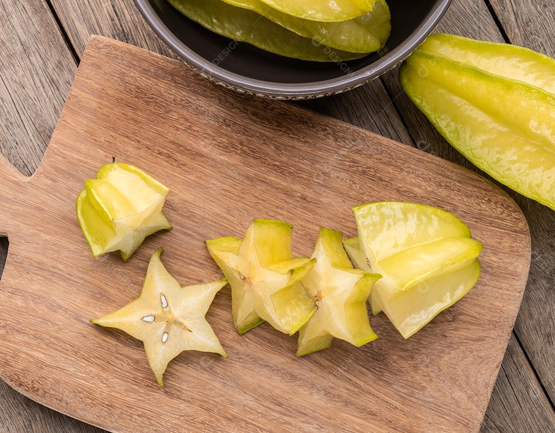 Carambolas com fatias em uma placa sobre a mesa de madeira.