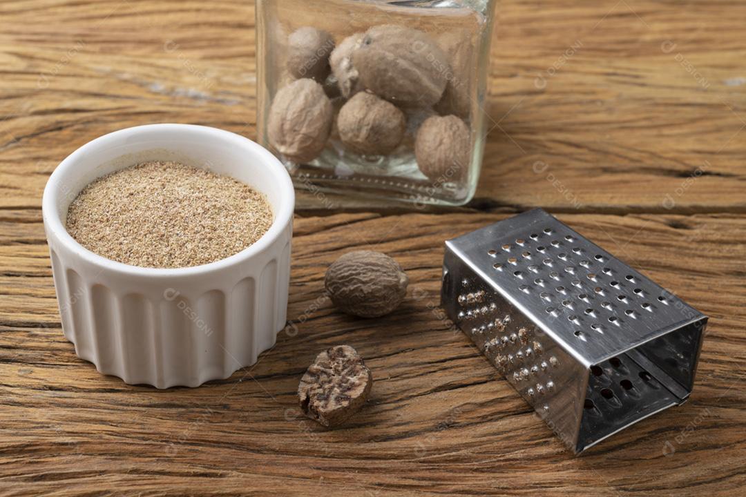 Noz-moscada com ralador sobre mesa wodden. Noz-moscada em pó em uma tigela