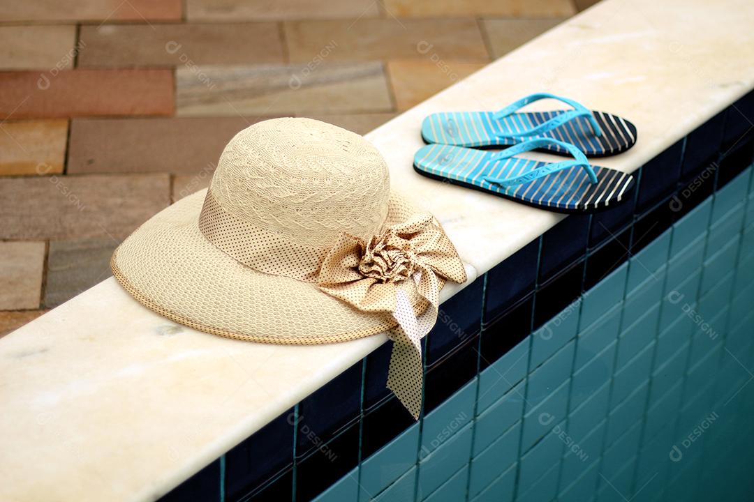 Chapeús palha chinelo sobre beira de piscina