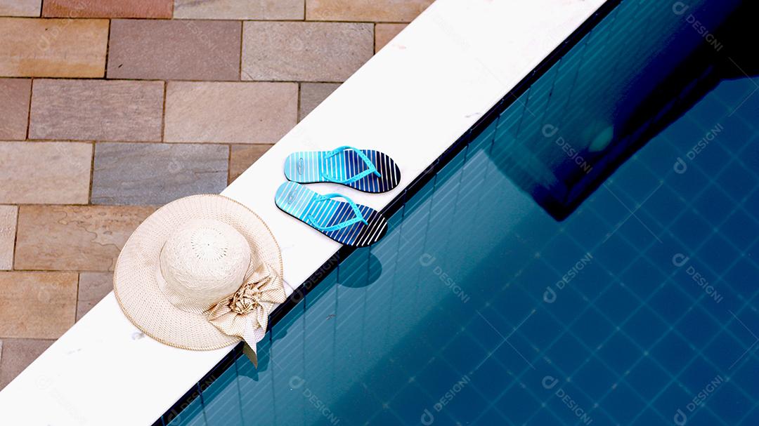 Chapeús palha chinelo sobre beira de piscina