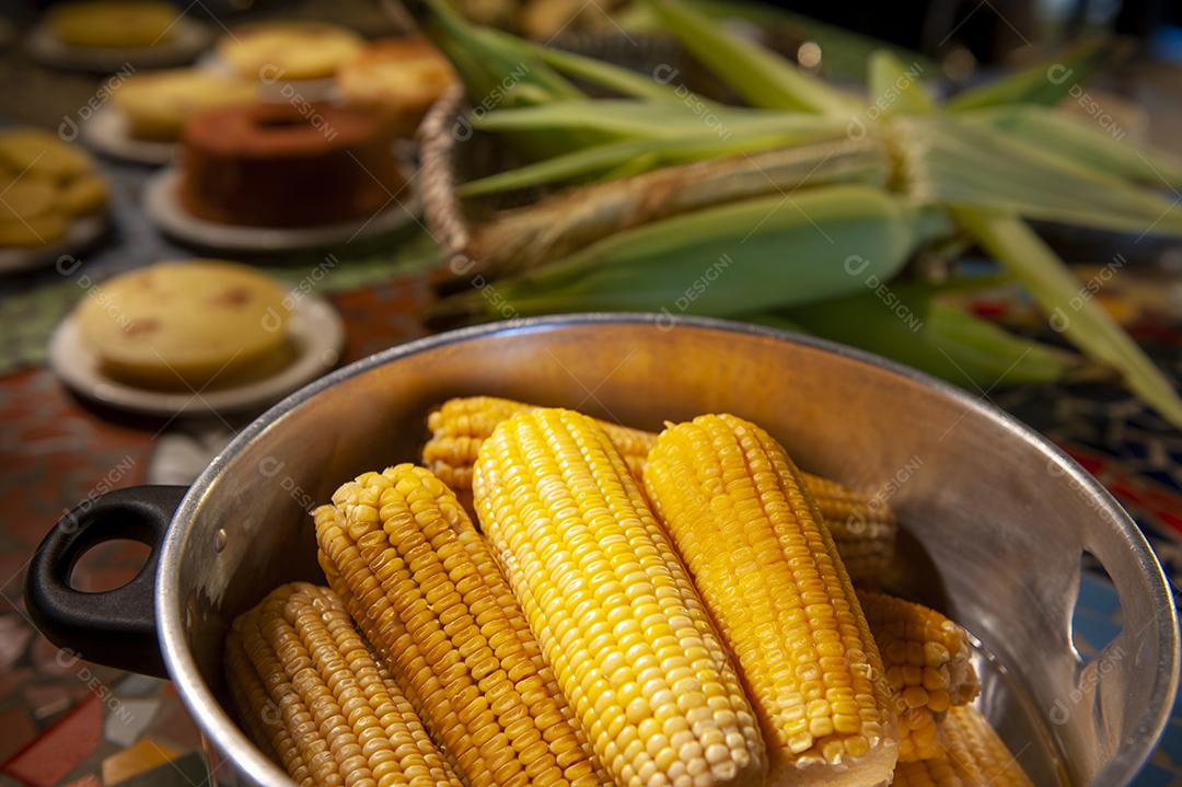 Milho cozido em uma mesa com outros alimentos feitos com milho no fundo desfocado. Culinária nordestina.