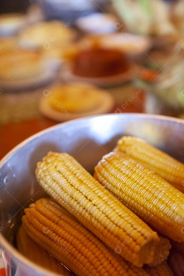Milho cozido em uma mesa com outros alimentos feitos com milho no fundo desfocado. Culinária nordestina.
