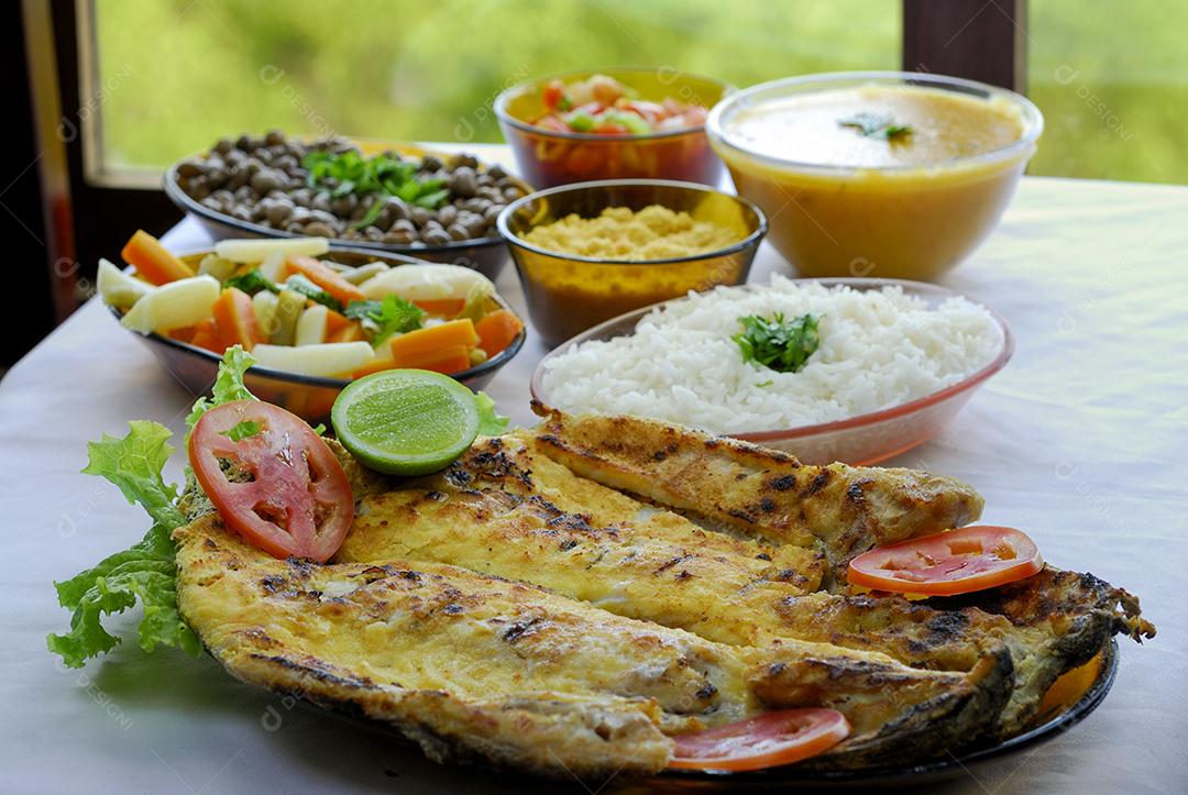 Filé de tilápia grelhado na mesa, servido com feijão, arroz, farofa, mingau e vinagrete. cozinha brasileira.