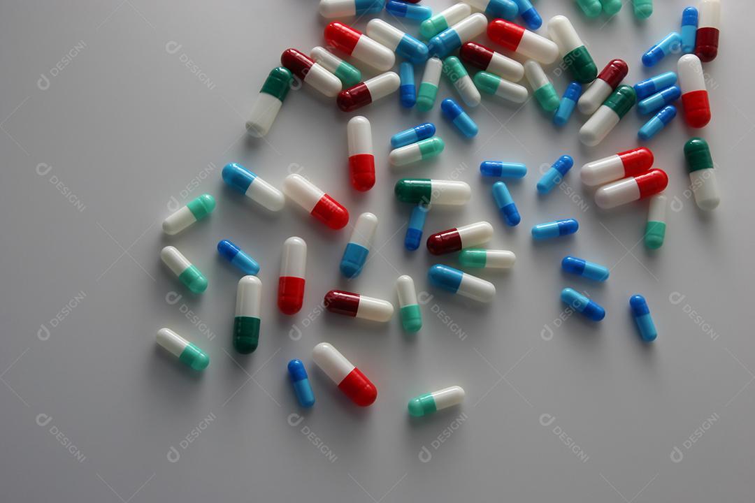 Comprimidos médicos em cores vermelhas, azuis, verdes e outras. Comprimidos soltos na superfície branca. Saúde e medicina.