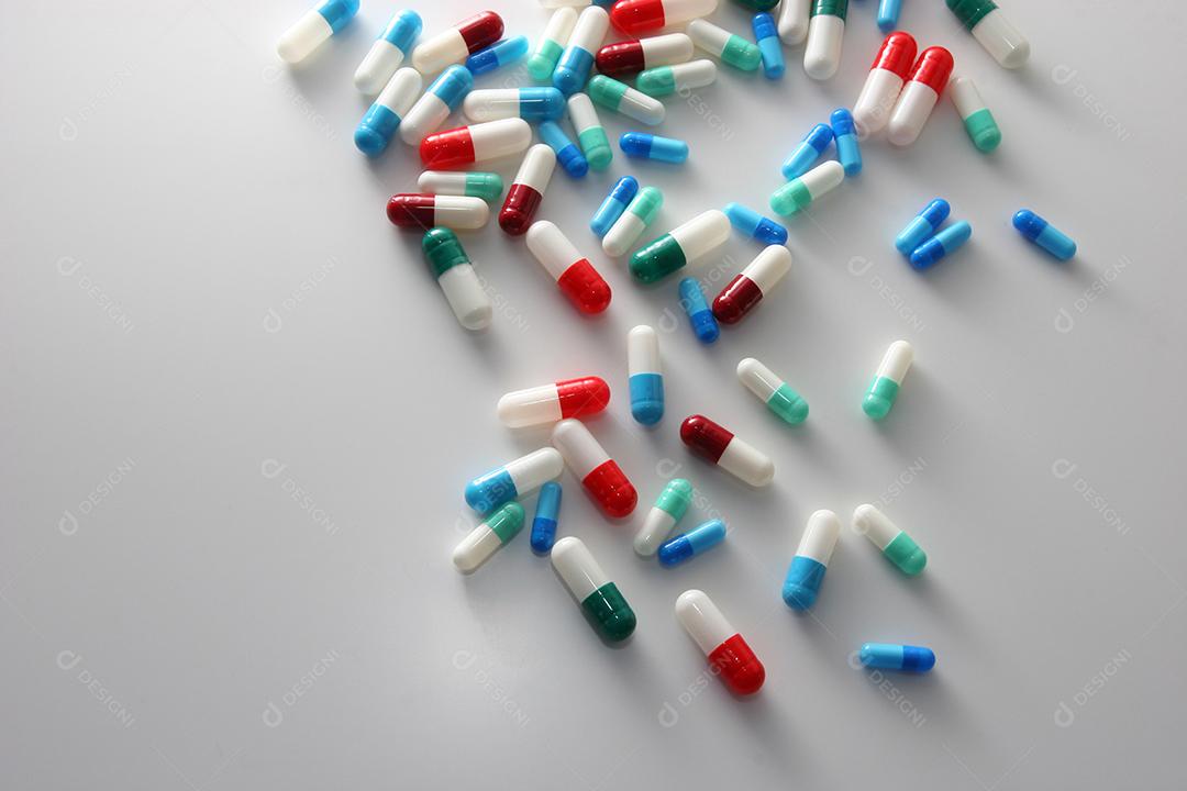 Comprimidos médicos em cores vermelhas, azuis, verdes e outras. Comprimidos soltos na superfície branca. Saúde e medicina.