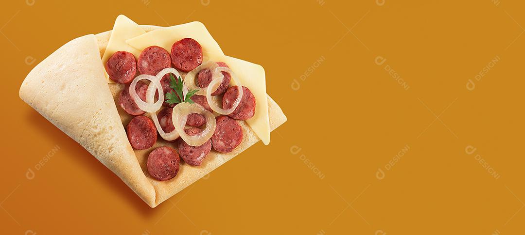 VISTA SUPERIOR DE CREPE OU PANQUECA FINA com fatias de linguiça calabresa COM cebola, salsa e queijo EM FUNDO DE LARANJA.