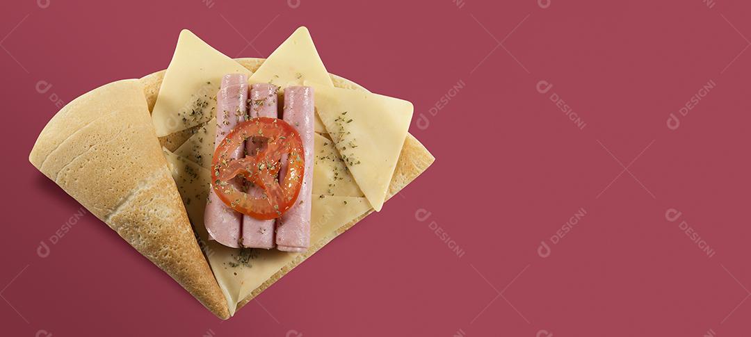 VISTA SUPERIOR DO CREPE OU PANQUECA FINA com fatia de tomate, presunto, queijo e orégano EM UM FUNDO VERMELHO CARIMBO.