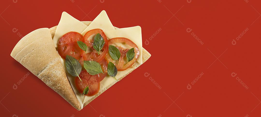 VISTA SUPERIOR DO CREPE OU PANQUECA FINA sabor marguerita com fatias de tomate, manjericão, queijo EM UM FUNDO VERMELHO.