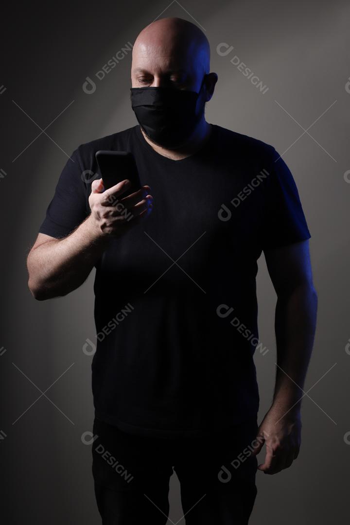 homem careca com camiseta preta usando máscara protetora nas costas cinza