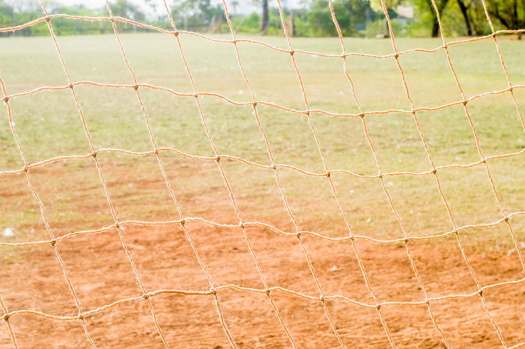 Textura com rede de futebol, luz do dia, grama, terra ao fundo.