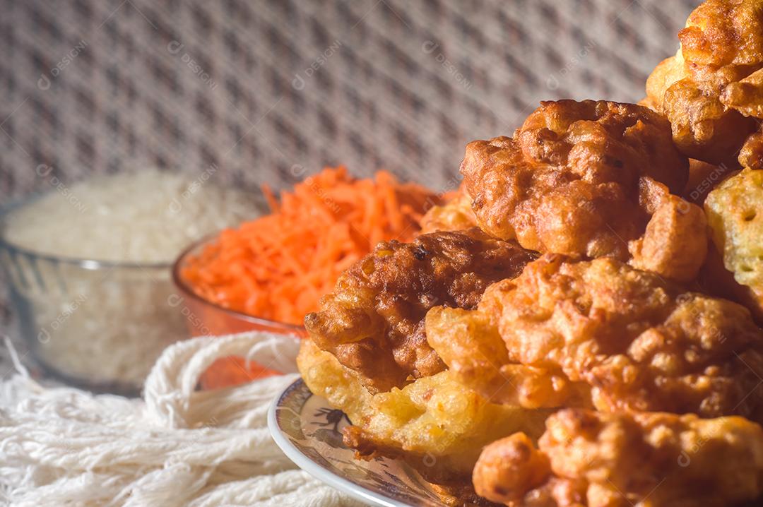 bolinhos de arroz fritos em um prato e fundo listrado, tigela com feijão