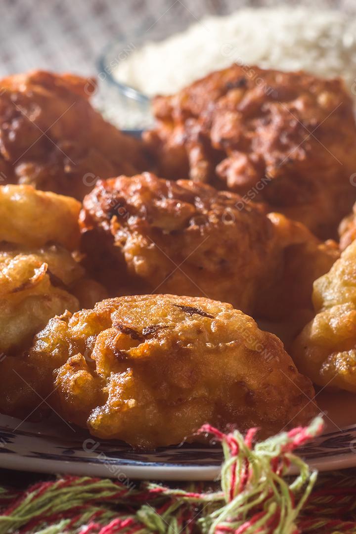 bolinhos de arroz fritos em um prato com espaço para texto e fundo listrado, tigela com feijão