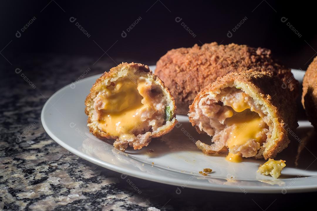 Bolinhos de salsicha com queijo cheddar e em uma placa de aço e mão segurando, fundo escuro