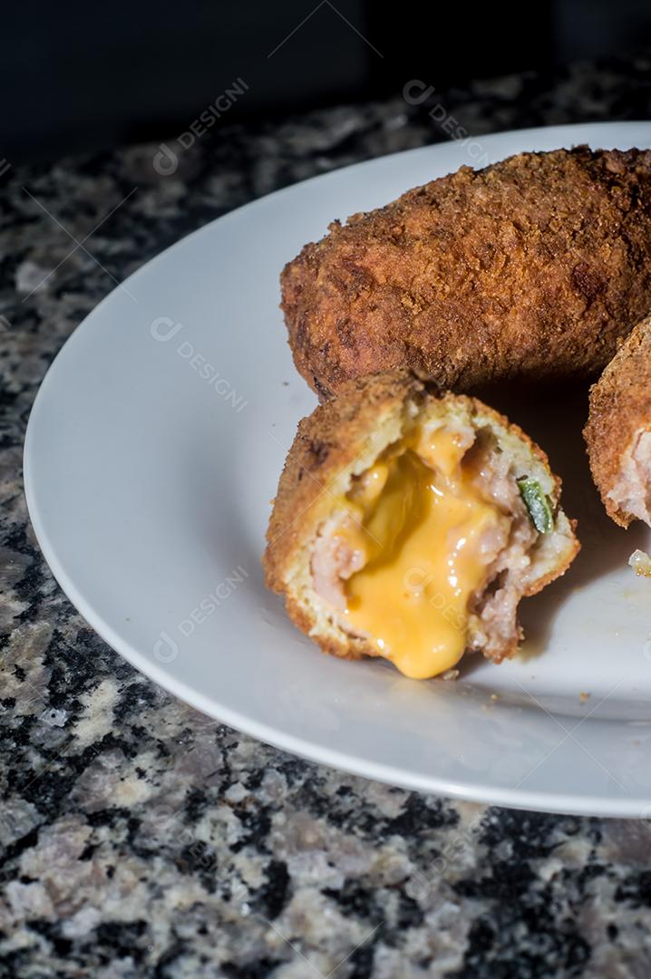 Bolinhos de salsicha com queijo cheddar e em uma placa de aço e mão segurando, fundo escuro
