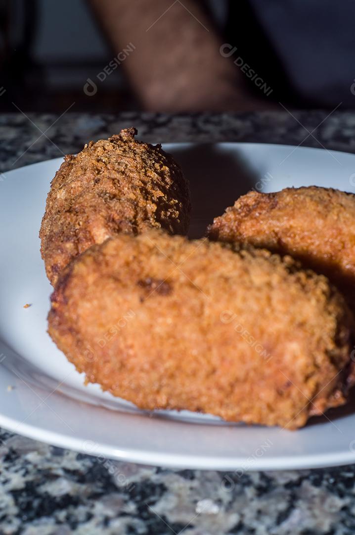 Bolinhos de salsicha com queijo cheddar e em uma placa de aço e mão segurando, fundo escuro