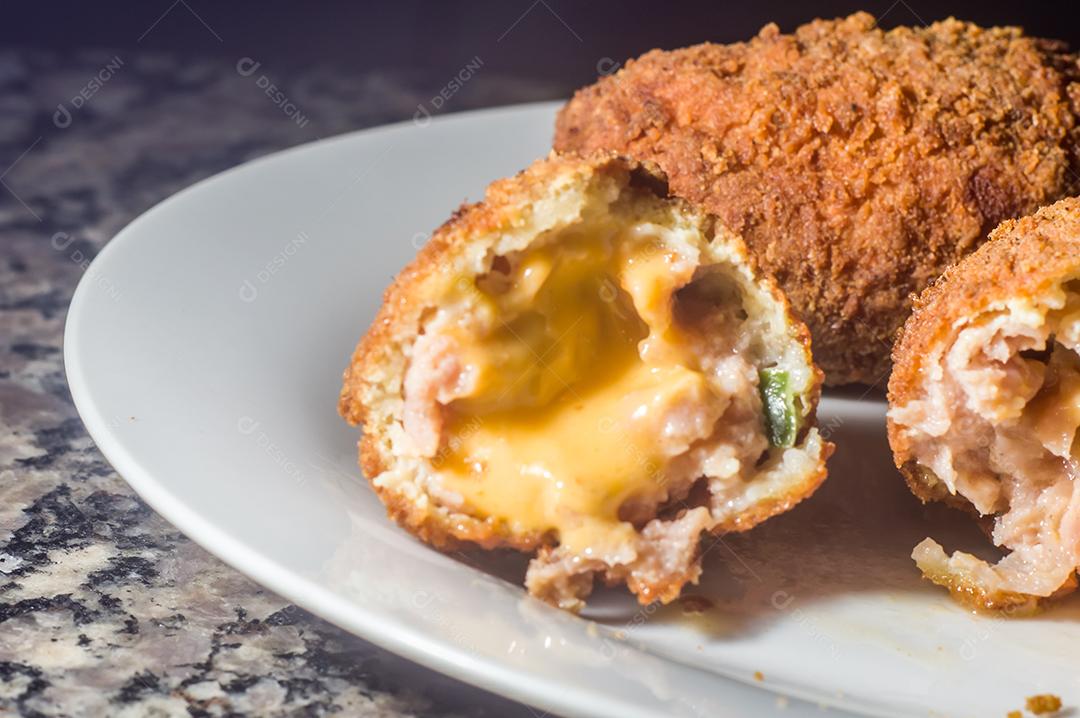 Bolinhos de salsicha com queijo cheddar e em uma placa de aço e mão segurando, fundo escuro