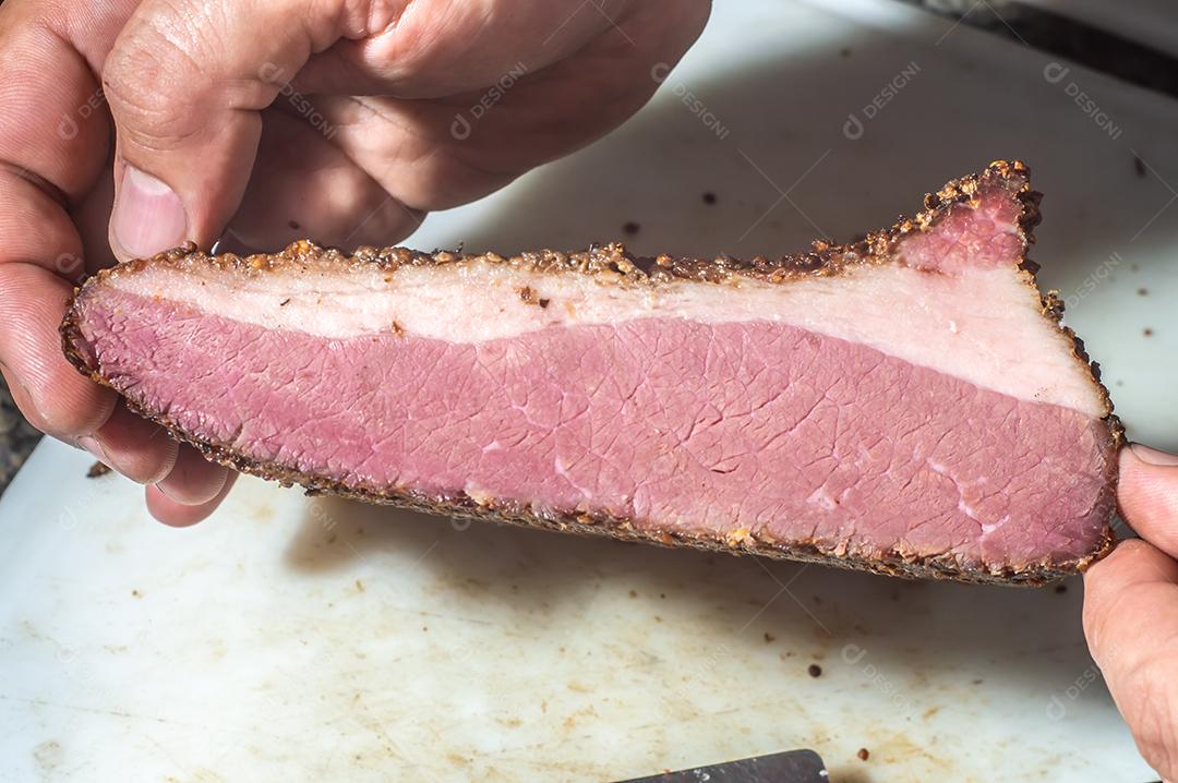 Carne assada, pastrami na tábua de ardósia, mão masculina segurando um pedaço de pastrami