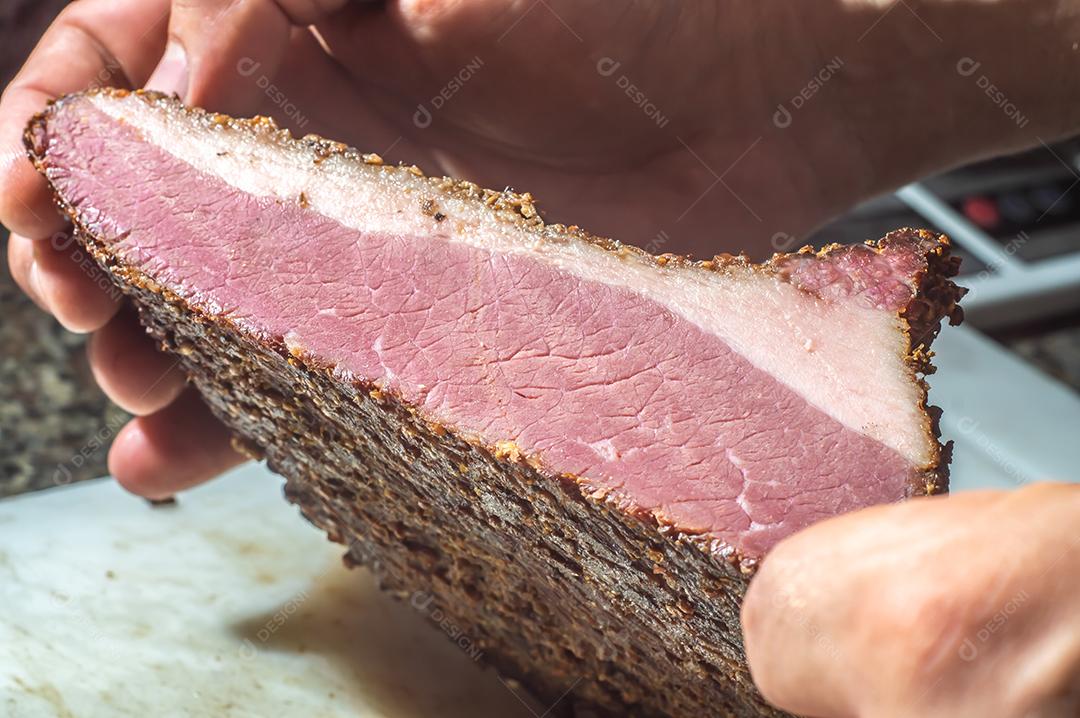 Carne assada, pastrami na tábua de ardósia, mão masculina segurando um pedaço de pastrami