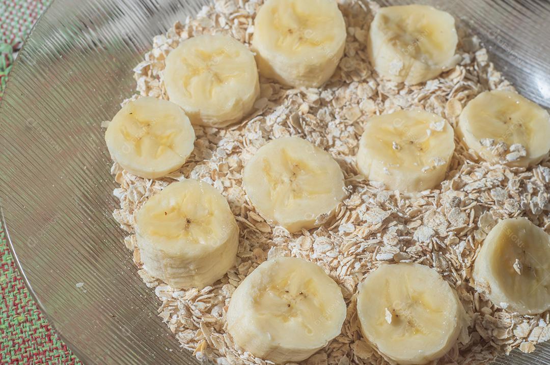 flocos de aveia e banana fatiada, em um prato que está em uma mesa com luz natural