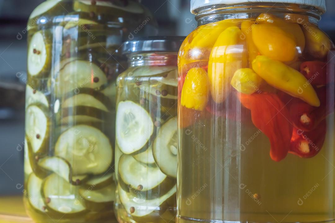 Pimentões amarelos enlatados e pepino em uma jarra em fundo de madeira, luz natural.