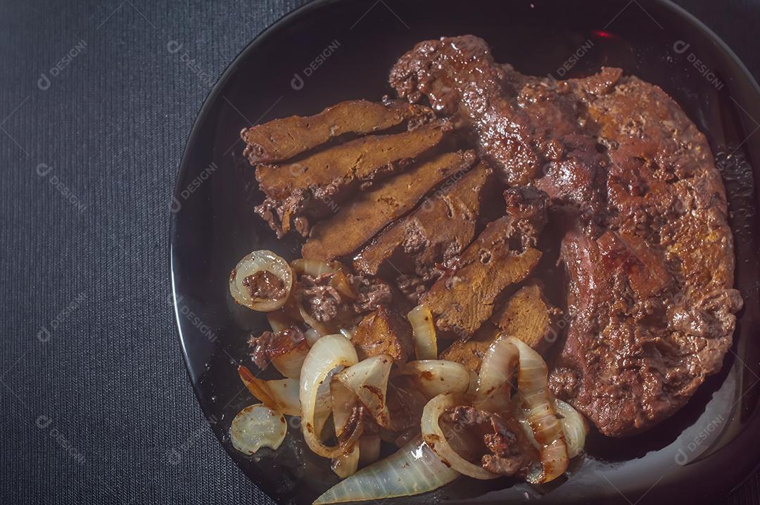 Fígado de boi frito, comida brasileira e colocado em um prato preto com cebola