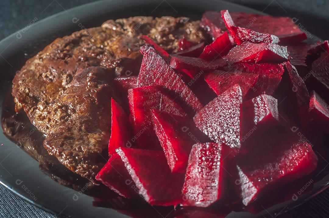 Fígado de boi frito, comida brasileira e colocado em um prato preto com cebola