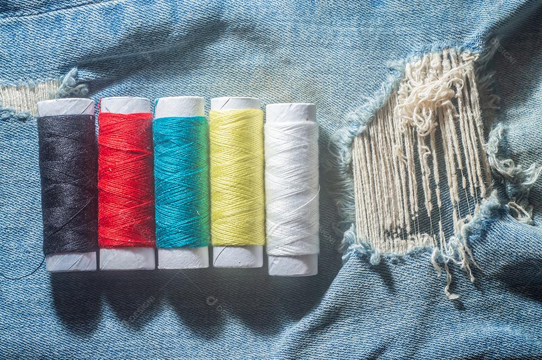 Bobinas com linhas de costura coloridas com jeans ao fundo, conceito de costura