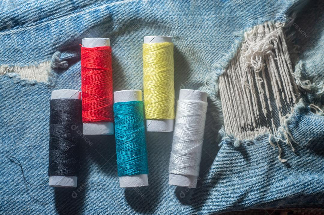 Bobinas com linhas de costura coloridas com jeans ao fundo, conceito de costura