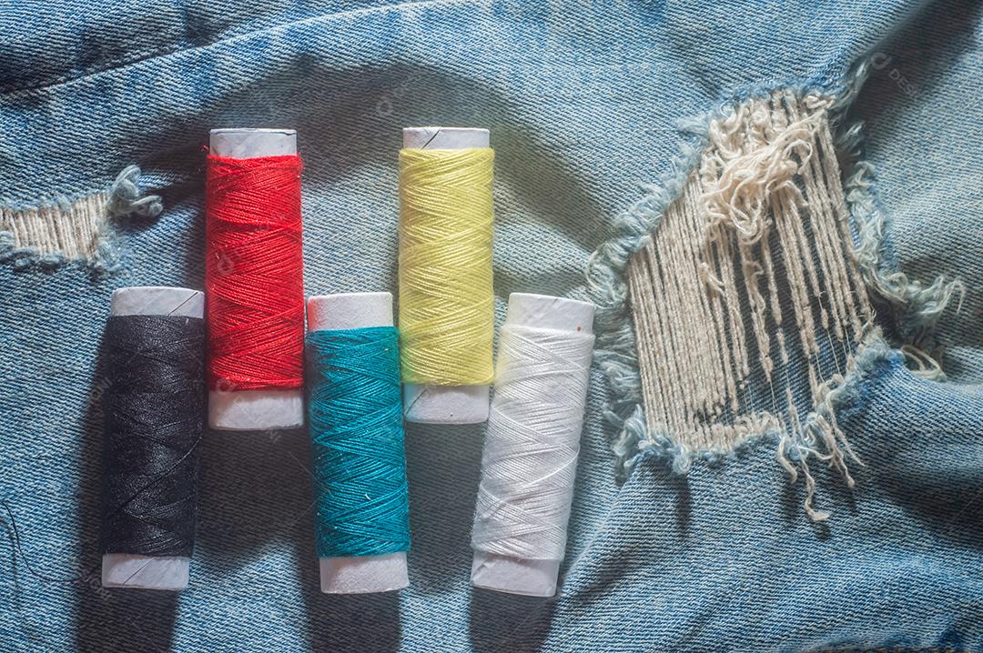 Bobinas com linhas de costura coloridas com jeans ao fundo, conceito de costura