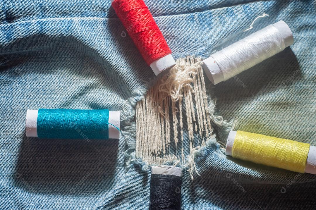 Bobinas com linhas de costura coloridas com jeans ao fundo, conceito de costura